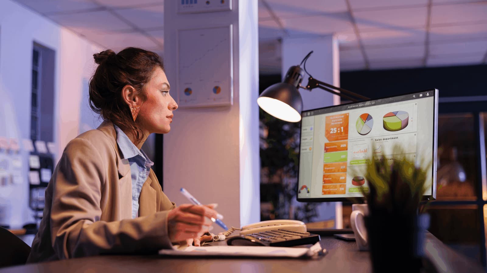 A marketing professional reviewing a business analytics dashboard on a monitor in a dimly lit office at night