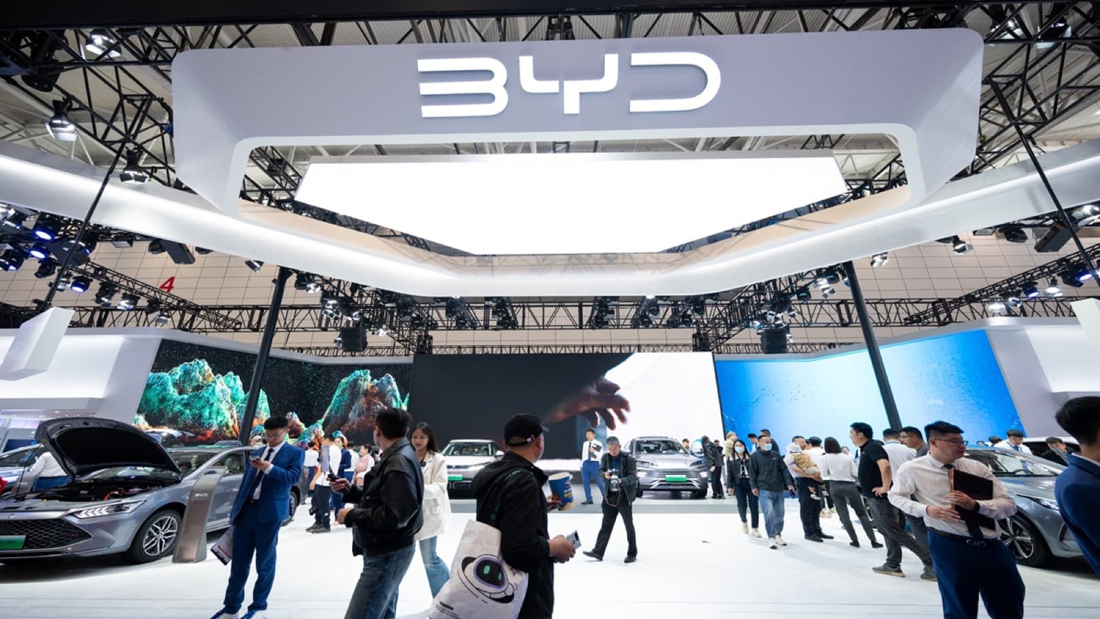 Visitors walk through a large BYD booth with the illuminated BYD logo overhead at an auto show