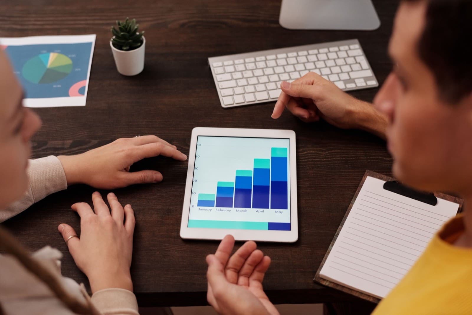 Two marketers reviewing a rising bar chart on a tablet while analyzing search performance