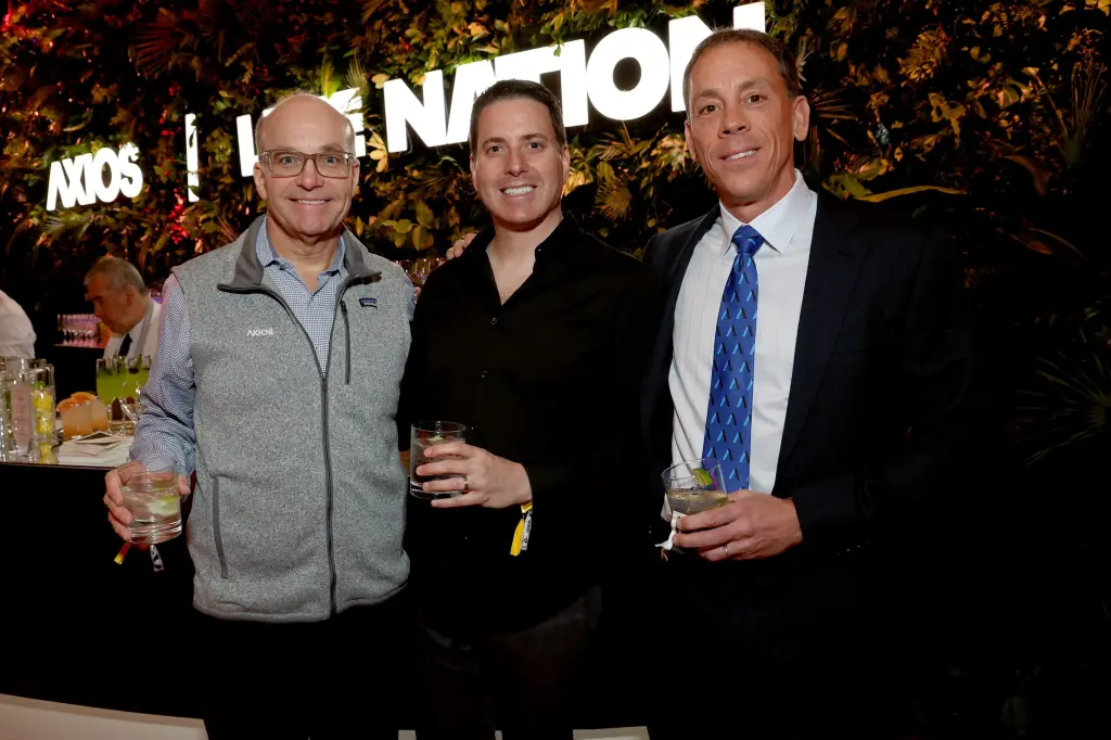 Three men in suits and casual jackets smiling and holding drinks in front of an Axios and Live Nation backdrop