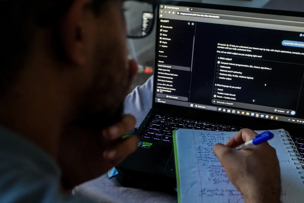 A person looking at a ChatGPT conversation on a laptop while writing notes