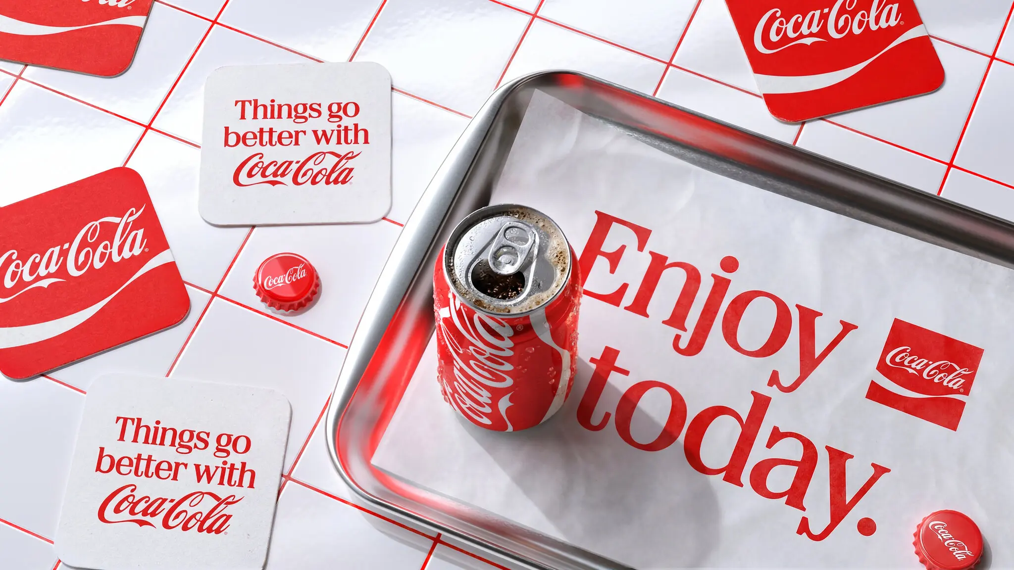 New Coca-Cola visual identity with an Enjoy today headline and retro Things go better with Coca-Cola coasters on a red and white tiled surface