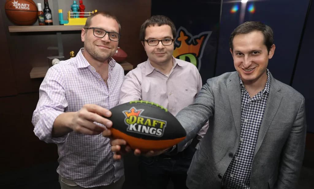Three DraftKings executives smiling and holding a branded football in an office setting