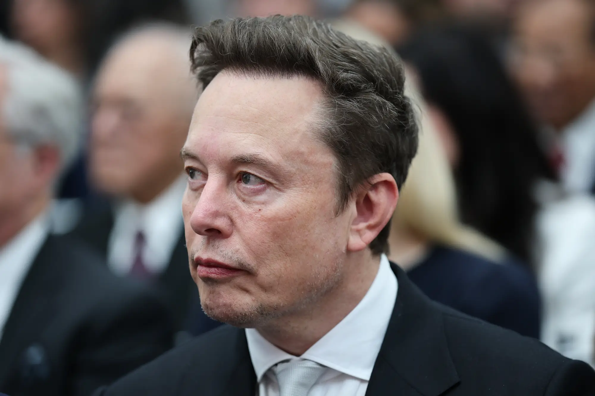Elon Musk looking to the side in a crowd