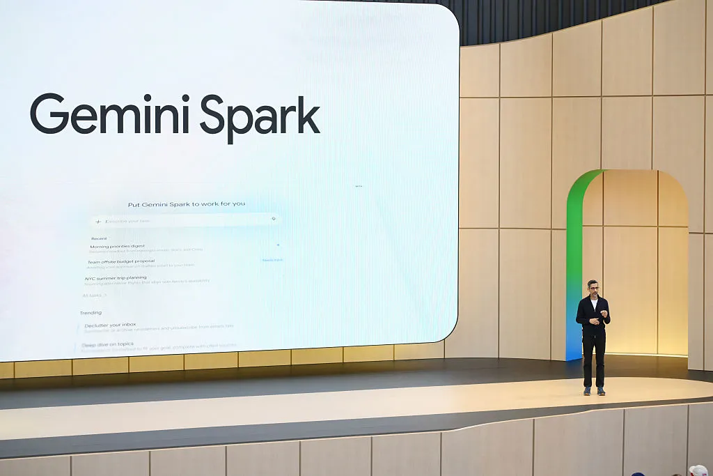 A Google executive on stage in front of a large screen displaying the Gemini Spark product name and interface