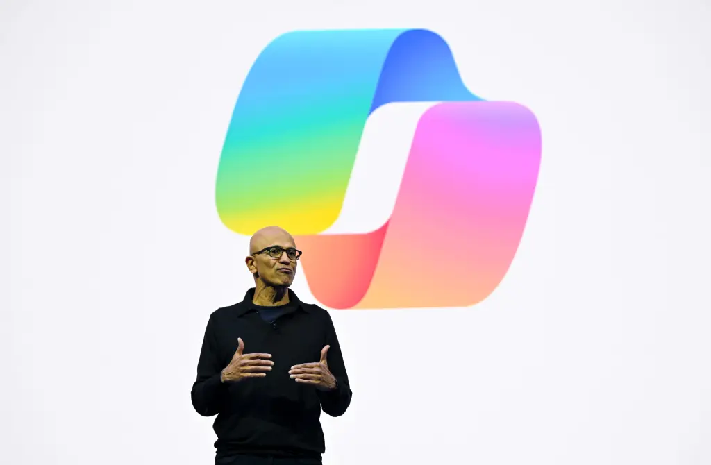 Satya Nadella speaking on stage in front of a large Microsoft Copilot logo