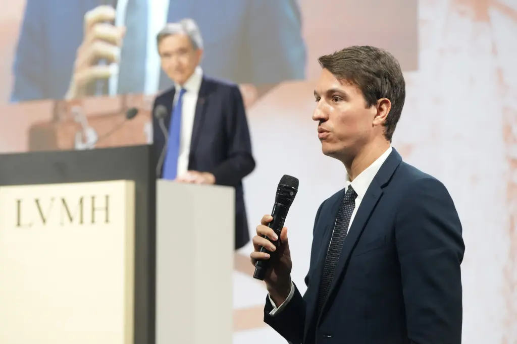 Alexandre Arnault speaking into a microphone on stage in front of an LVMH podium and screen