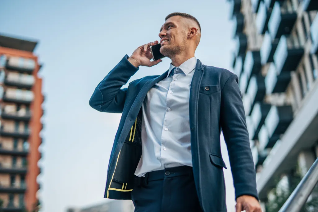 A man in a suit smiling while talking on his phone outside an office building