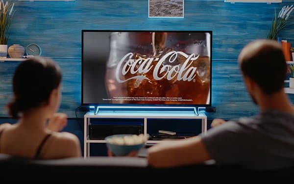 A couple watching a soft drink commercial on a large living room television screen